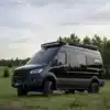 Schwarzer Mercedes Sprinter 144 HR 4x4 Campervan mit Dachträger und Offroad-Ausstattung auf einer Wiese
