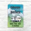 Buntes Blechschild mit Wohnwagen und dem Spruch 'Zuhause ist dort, wo wir parken', personalisiert mit Namen, vor weißer Wand