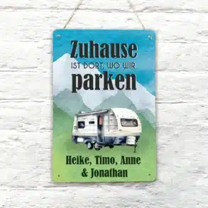 Buntes Blechschild mit Wohnwagen und dem Spruch 'Zuhause ist dort, wo wir parken', personalisiert mit Namen, vor weißer Wand