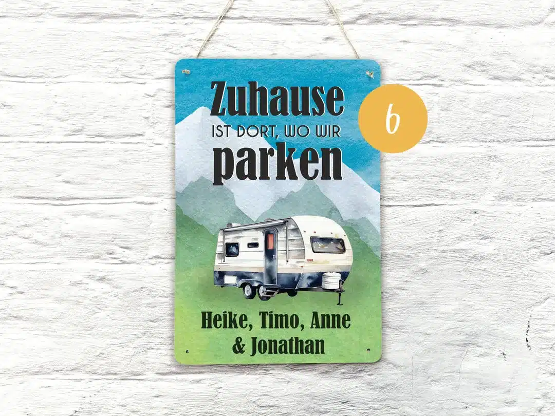 Buntes Blechschild mit dem Spruch 'Zuhause ist dort, wo wir parken', Wohnwagen-Illustration und personalisierten Namen, aufgehängt an einer weißen Wand
