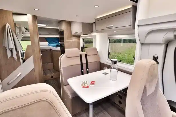 Innenansicht eines Carado T448 Wohnmobils mit Sitzgruppe, Tisch und Blick auf die Längseinzelbetten im Heck