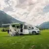 Carado V347 Campervan mit Markise, Familie sitzt davor auf einer Wiese mit Bergen im Hintergrund
