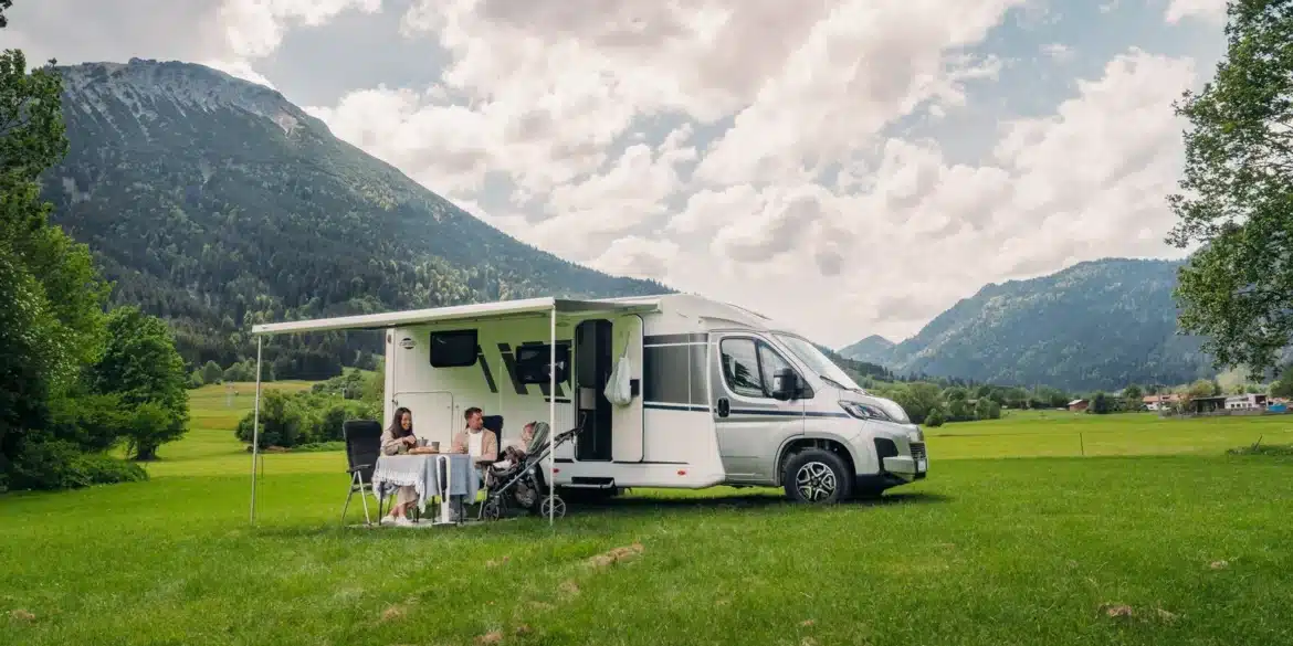Carado V347 Campervan mit Markise, Familie sitzt davor auf einer Wiese mit Bergen im Hintergrund