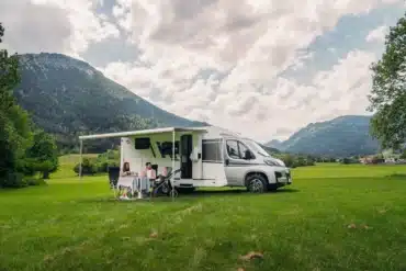 Carado V347 Campervan mit Markise, Familie sitzt davor auf einer Wiese mit Bergen im Hintergrund