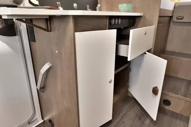 Geöffnete Schranktüren und Schublade unter der Küchenarbeitsplatte im Carado V347 Wohnmobil