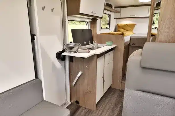 Blick in den Innenraum eines Carado V347 Vans mit Küchenzeile, Sitzgruppe und Längsbetten im Heck