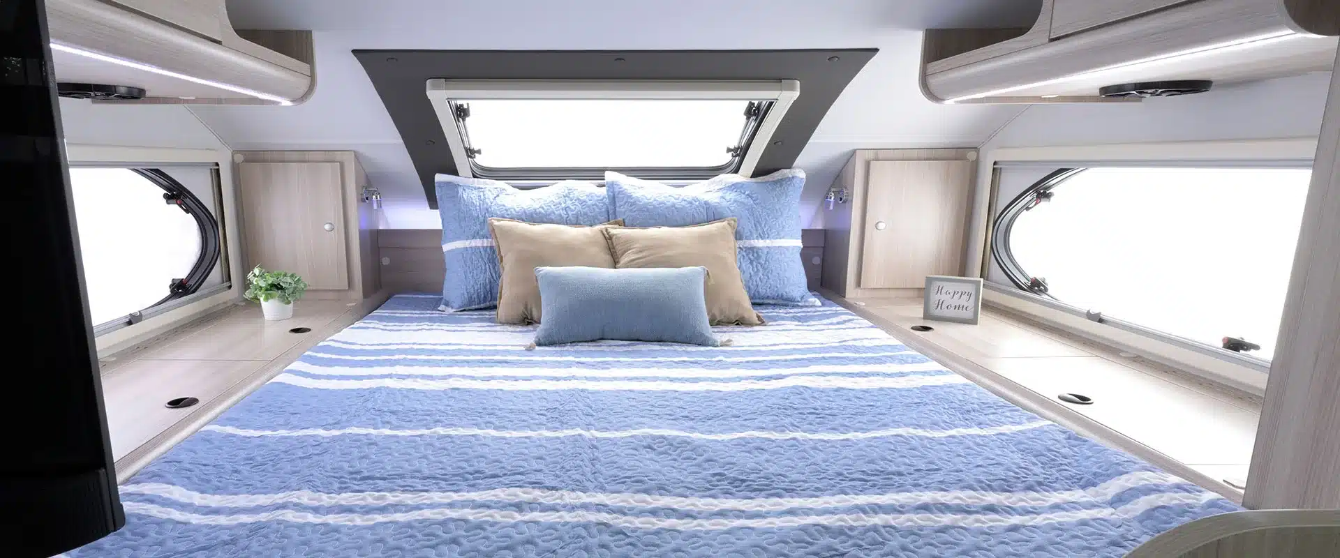 Innenansicht des Schlafbereichs im Cirrus 920 Truck Camper mit blau-weißem Bett, Fenstern und Stauraum