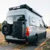 Heckansicht eines ausgebauten Mercedes Sprinter 170 4x4 Campervans mit Ersatzrad, Dachträger und Outdoor-Komponenten auf einem Feldweg