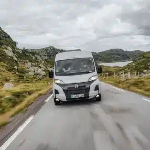 Frontansicht eines Crosscamp ADVTR 5.41 Camper-Vans auf einer kurvigen Landstraße in hügeliger Landschaft