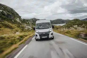 Frontansicht eines Crosscamp ADVTR 5.41 Camper-Vans auf einer kurvigen Landstraße in hügeliger Landschaft