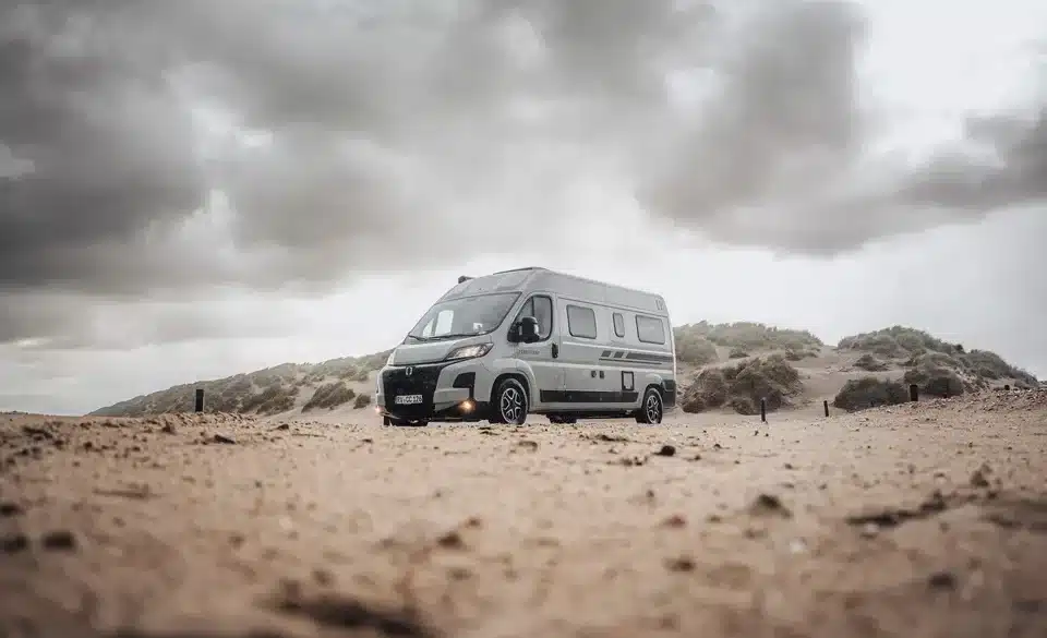 CROSSCAMP ADVTR 6.4 EF Kastenwagen-Camper steht auf sandigem Untergrund vor bewölktem Himmel