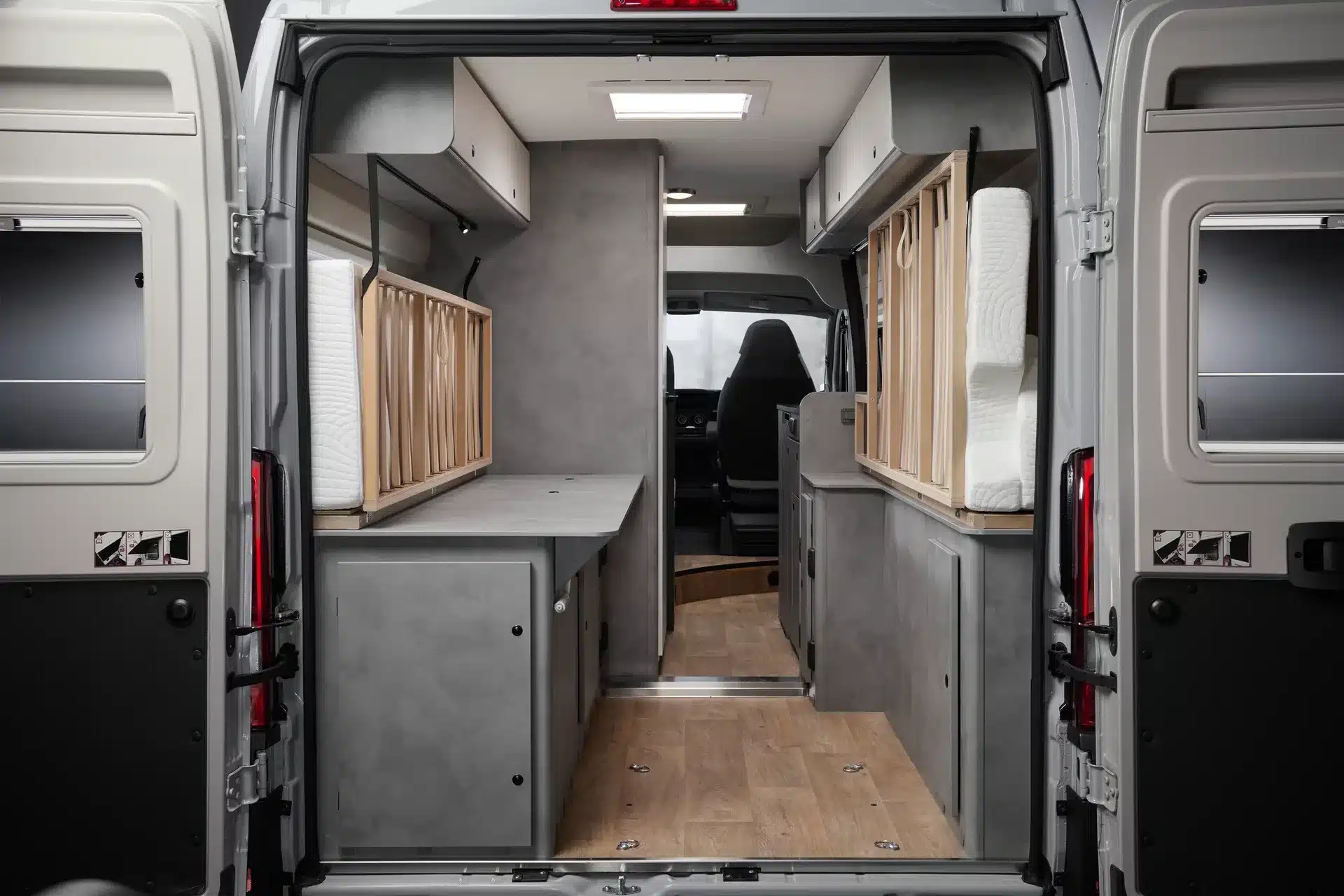 Blick in den Innenraum eines CROSSCAMP ADVTR 6.4 EF Kastenwagen-Campers mit hochgeklappten Längsbetten, viel Stauraum und moderner Ausstattung