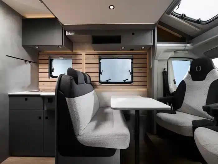 Innenansicht des Crosscamp EXPDN 7.4 E mit Halbdinette, Tisch, drehbaren Fahrersitzen und moderner Ausstattung