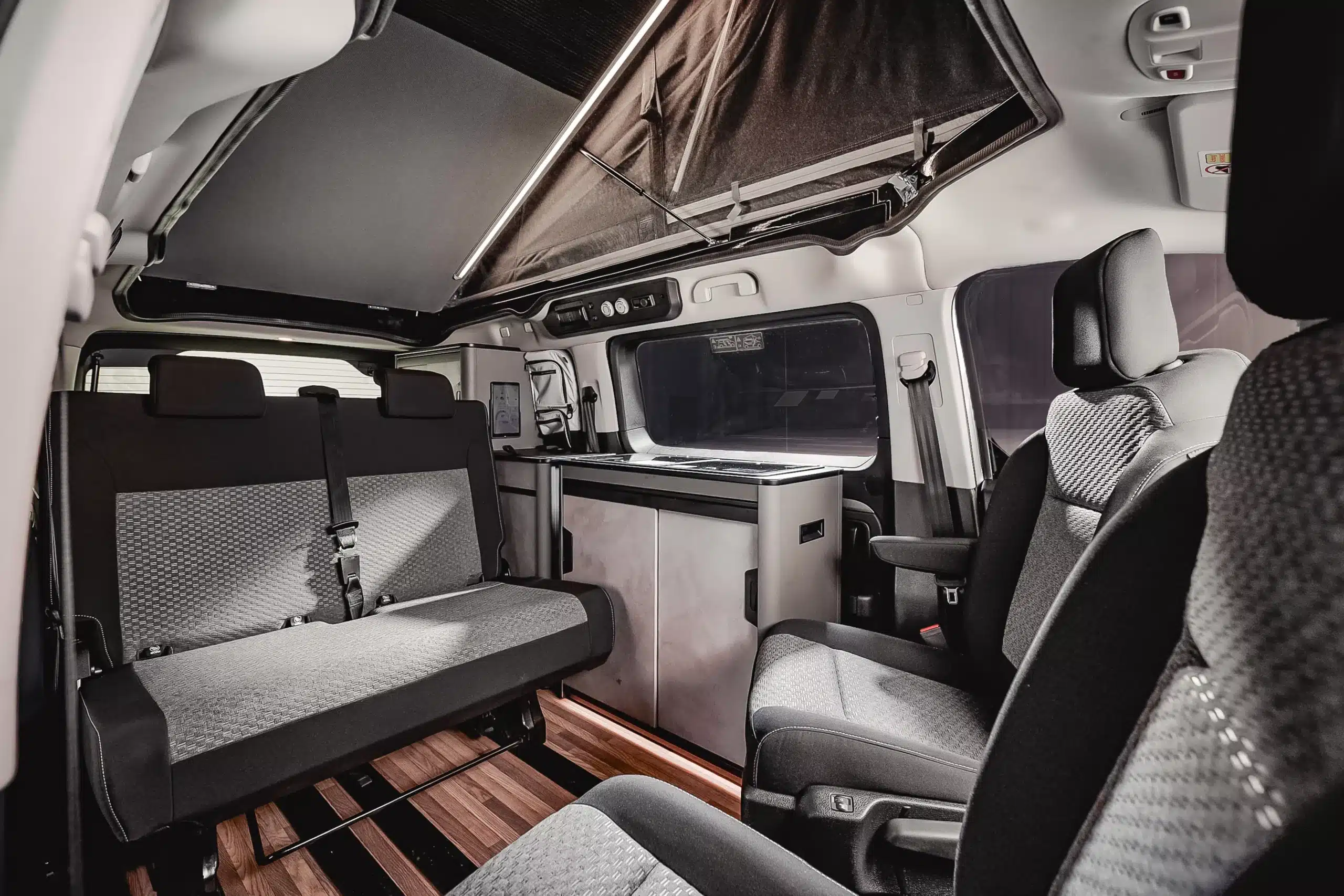 Innenansicht des Crosscamp EXPLR mit geöffneter Schlafdach-Koje, Sitzgruppe und Küchenzeile