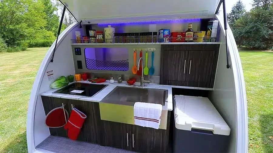 Outdoor-Küche eines inTech Luna Teardrop Trailers mit Edelstahlspüle, Kochfeld, Schränken und Küchenutensilien