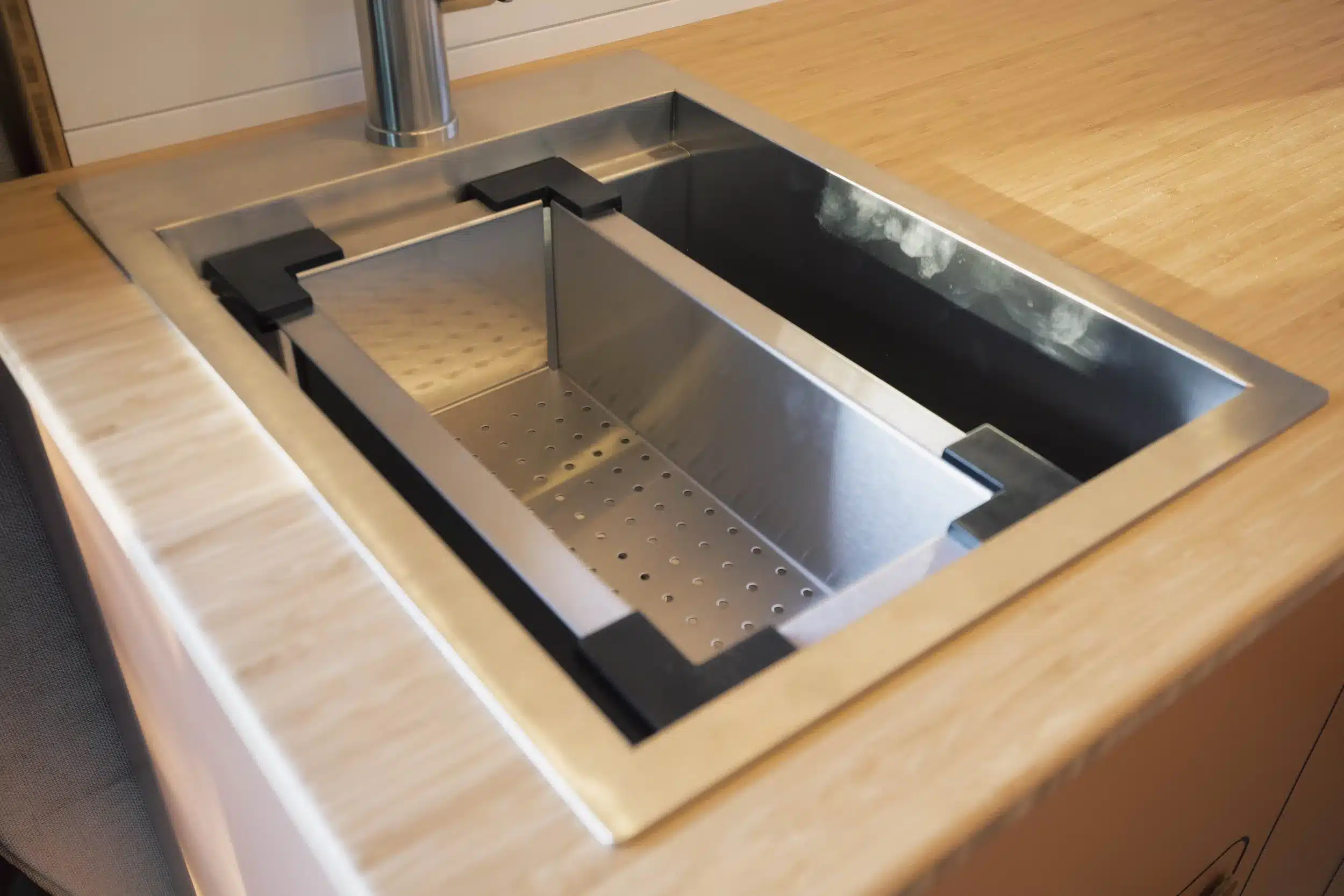 Modernes Edelstahl-Spülbecken mit integriertem Schneidebrett und Wasserhahn in einer Campervan-Küche mit Bambus-Arbeitsfläche