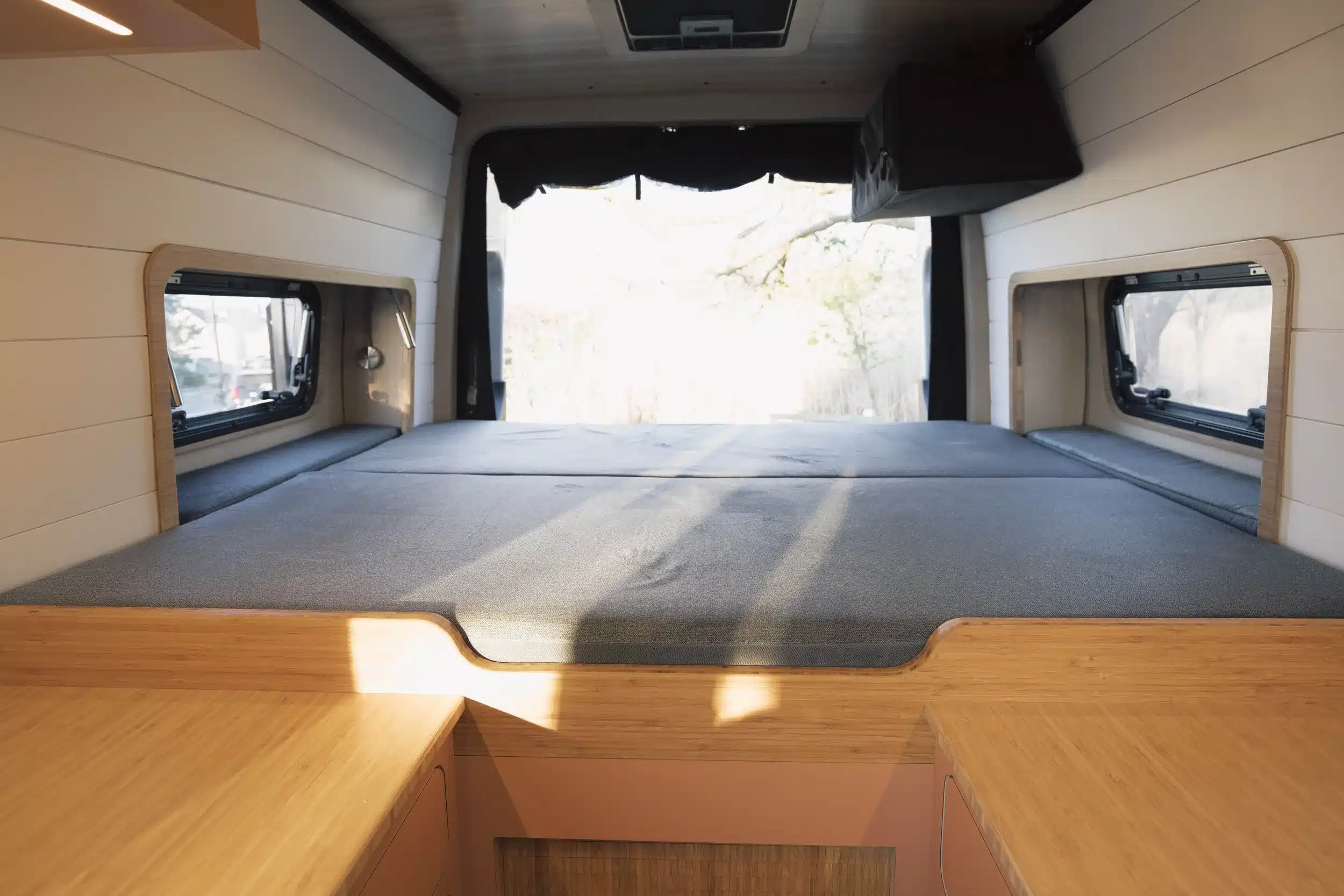 Innenraum eines Ocean-Side Campervans mit ausgeklapptem Bett, Holzverkleidung und seitlichen Fenstern