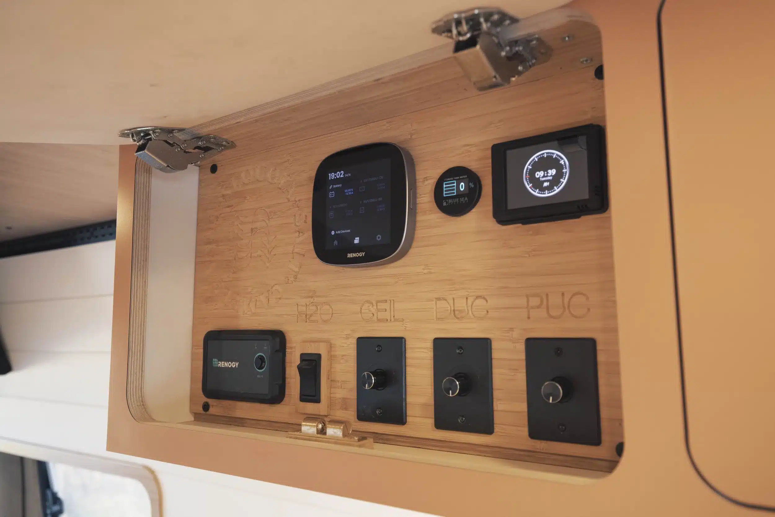 Detailaufnahme eines Steuerungspanels mit Displays und Schaltern im Ocean-Side Campervan, montiert auf einer Bambusplatte