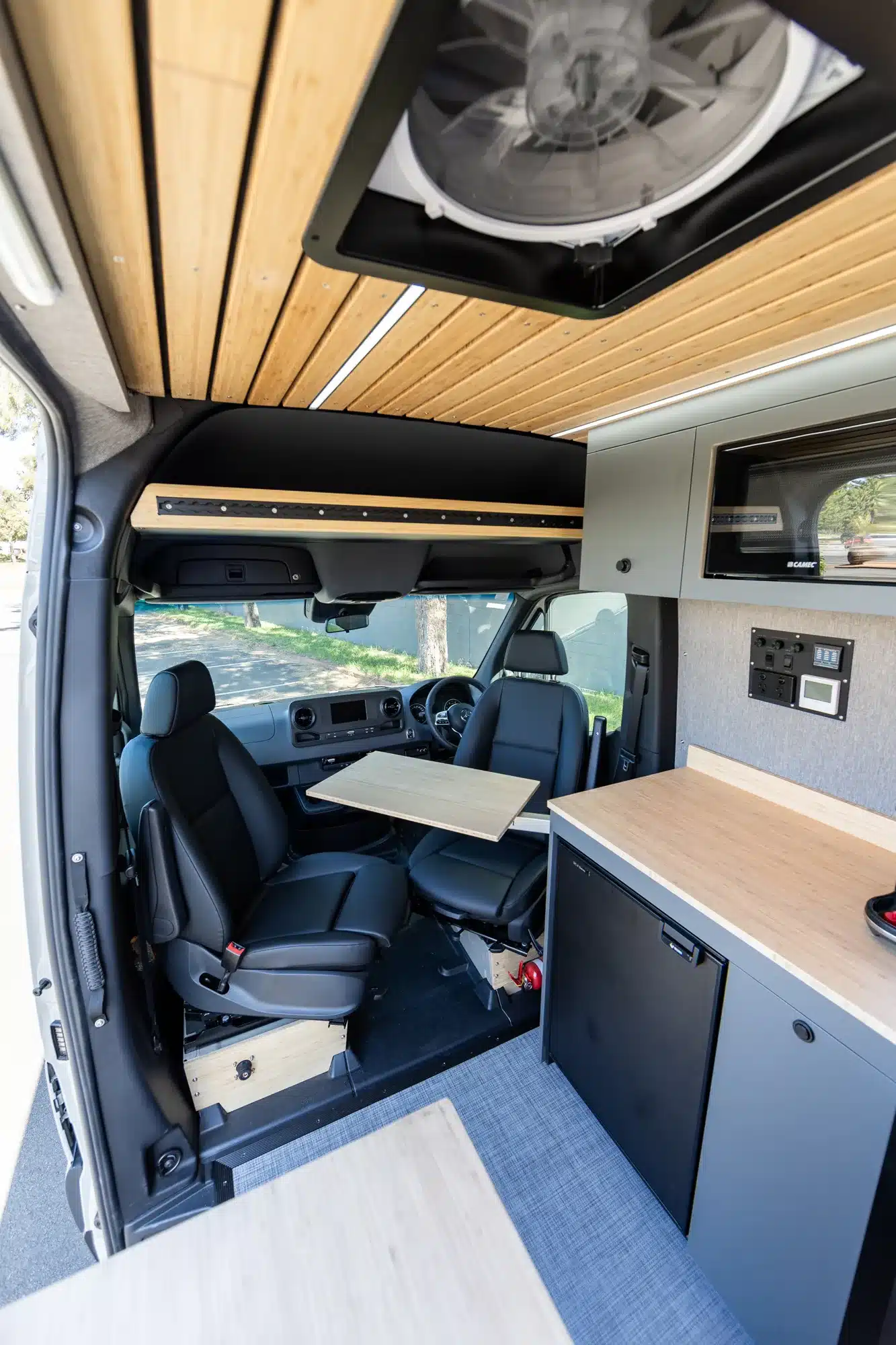Blick in den Innenraum eines Summit M1 Vans mit drehbaren Sitzen, Klapptisch, Küchenzeile, Holzdecke und modernen Einbauten