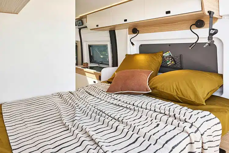 Innenansicht des Schlafbereichs im Kastenwagen V540G mit Querschläferbett, gelber Bettwäsche und Überkopf-Stauraum