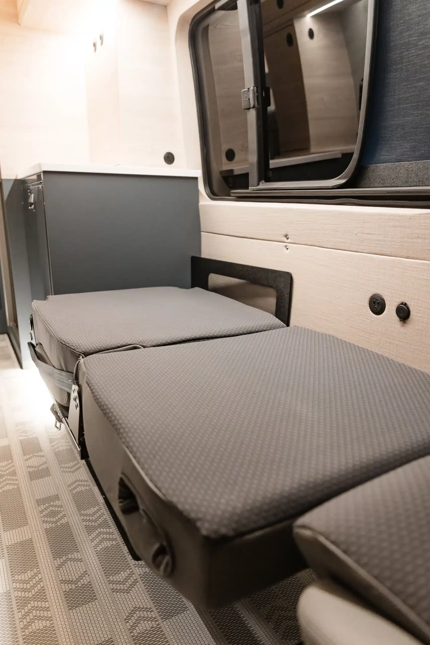 Innenansicht eines Campervans mit ausgeklapptem Bett und modernem Möbelbau