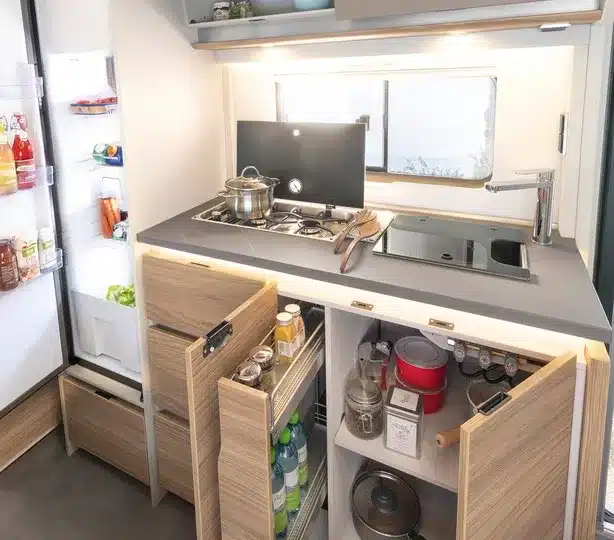 Innenansicht der modernen Wohnwagenküche im Dethleffs Nomad mit offenem Stauraum, Gasherd, Spüle und beleuchteter Küchenrückwand