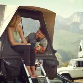 Zwei Personen sitzen entspannt im geöffneten Dometic TRT 140 AIR Dachzelt auf einem Fahrzeug, mit Blick auf eine Berglandschaft