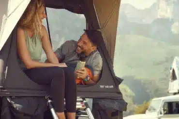 Zwei Personen sitzen entspannt im geöffneten Dometic TRT 140 AIR Dachzelt auf einem Fahrzeug, mit Blick auf eine Berglandschaft