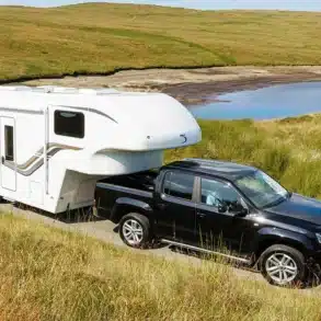 Dreamseeker Fifth Wheel Caravan wird von einem schwarzen Pick-up auf einer Landstraße in einer grünen Landschaft gezogen