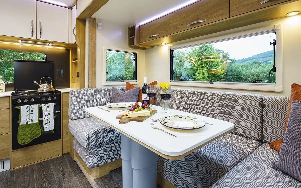 Innenansicht des Dreamseeker Fifth Wheel Caravan mit moderner Küche, Esstisch und gemütlicher Sitzgruppe vor großen Fenstern