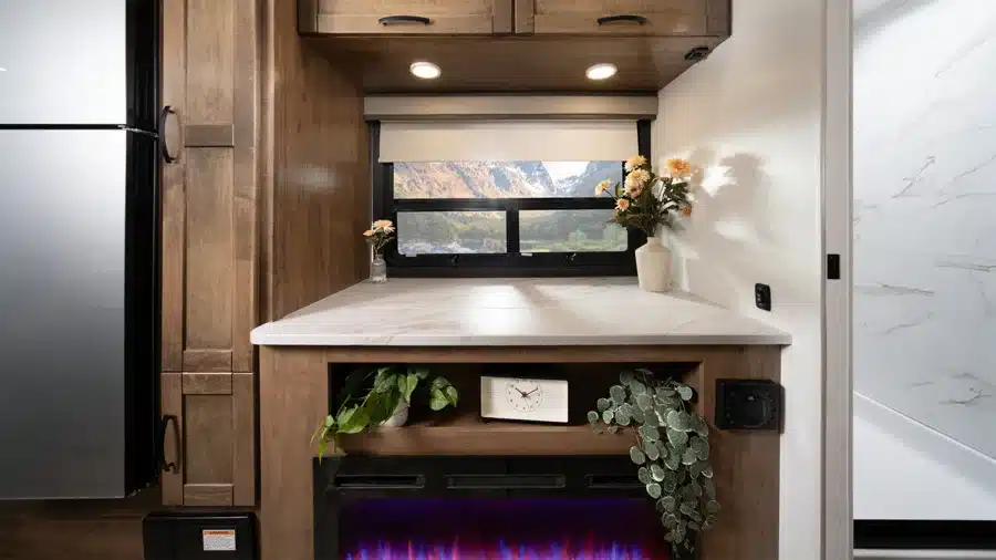Innenansicht des Entegra Coach Esteem XL mit Arbeitsfläche, Kamin, Pflanzen und Blick aus dem Fenster auf Berge
