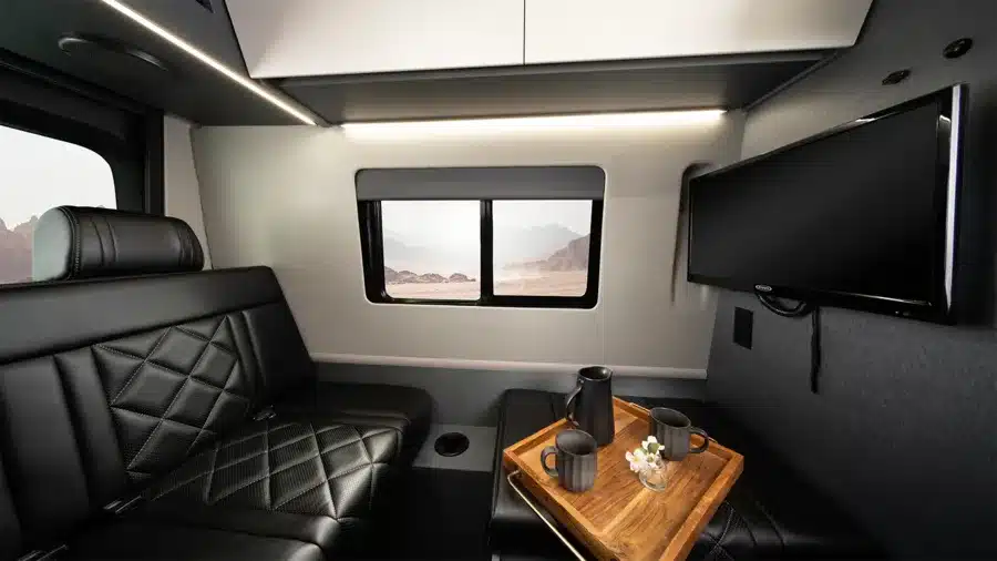 Innenansicht des Entegra Insignia Executive Vans mit schwarzer Ledersitzbank, Wandmonitor und Tablett mit Kaffeekanne