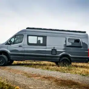 Seitenansicht eines grauen 2019 Mercedes Sprinter 170 EXT 4x4 Vans mit Offroad-Ausstattung auf einem Feldweg