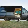 Seitenansicht eines For Adventure 2024 Sprinter AWD Campervans mit geöffneter Tür und Hund auf einer Wiese
