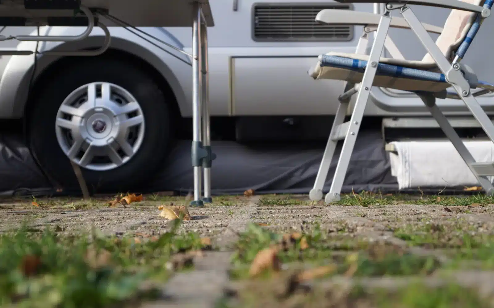 Wohnmobil mit montierter aufblasbarer Bodenschürze GentleTent Seal Tube auf einem Campingplatz, im Vordergrund Campingmöbel