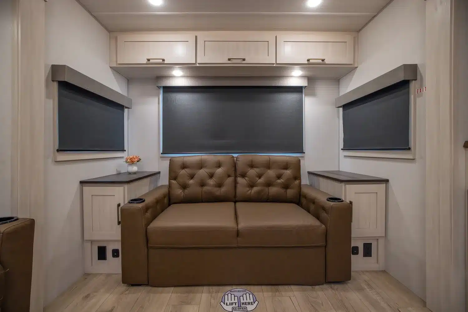 Modern eingerichteter Wohnbereich mit braunem Sofa, Stauraum und Verdunkelungsrollos im Grand Surveyor 305RLBS Travel Trailer