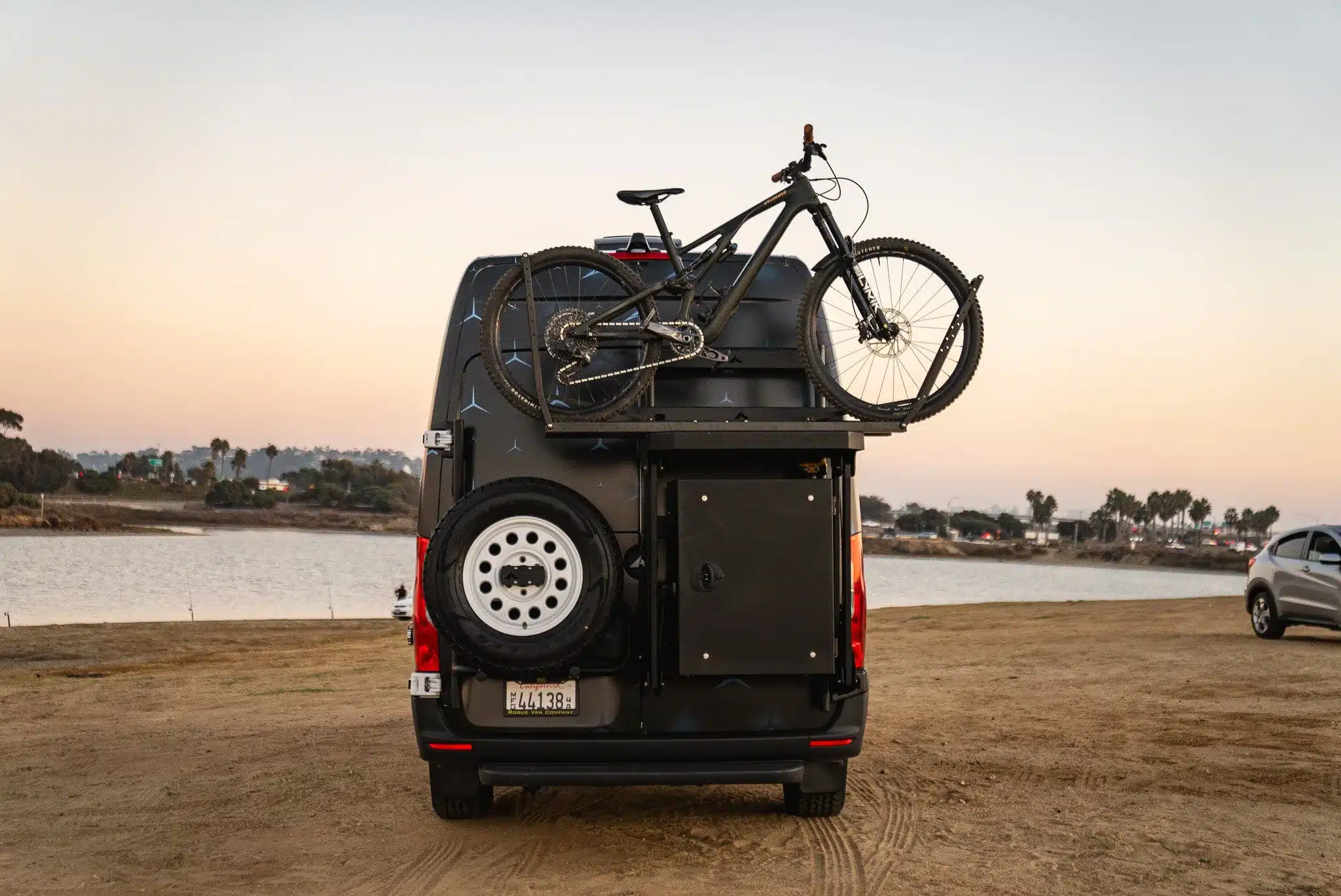 Heckansicht eines GridRunner eSprinter mit montiertem Fahrrad und Ersatzrad am Seeufer bei Sonnenuntergang