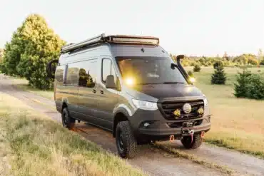 Gus 4x4 Sprinter Campervan mit Offroad-Umbau, Dachträger, Zusatzbeleuchtung und grobstolligen Reifen auf einem Feldweg