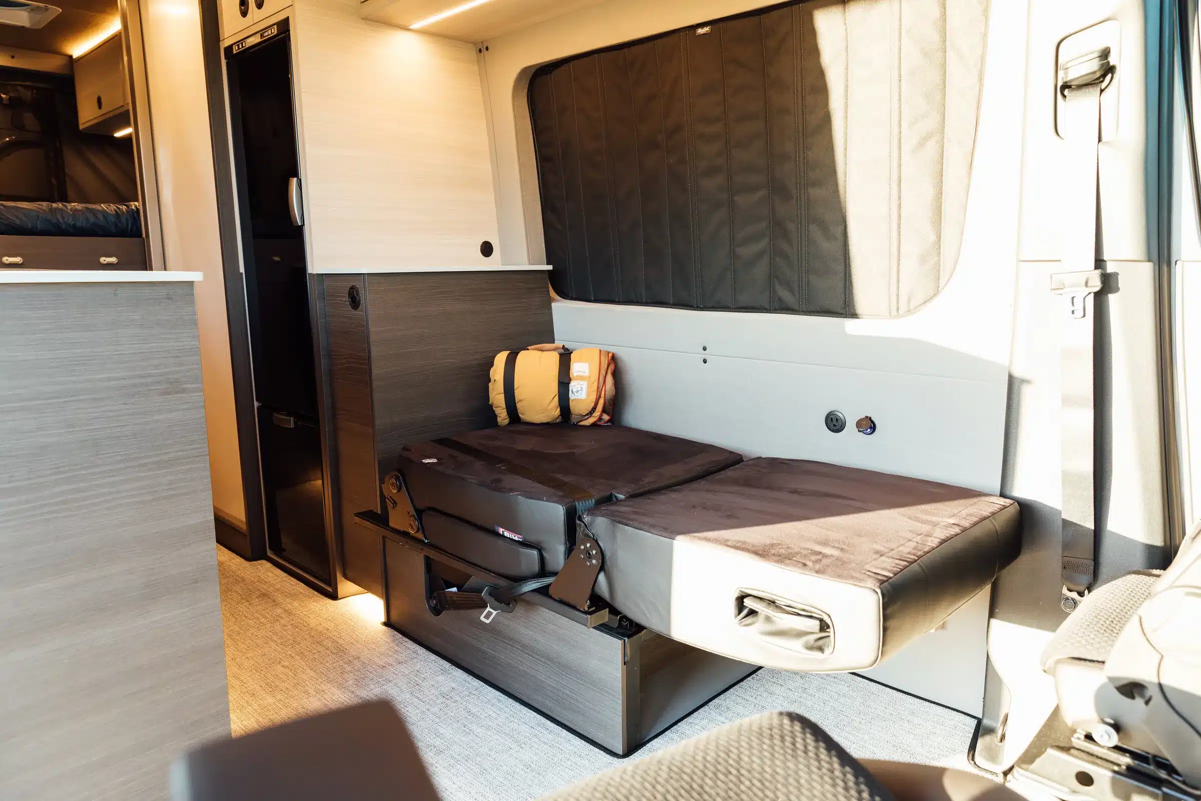 Innenansicht des Gus 4x4 Sprinter Campervan mit ausgeklapptem Sitz- und Schlafbereich, modernen Möbeln und Stauraum