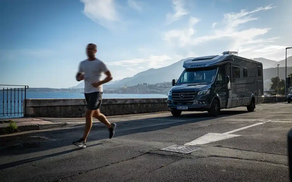 HYMER B-Klasse MasterLine T Wohnmobil steht an einer Küstenstraße mit Meerblick, im Vordergrund joggt eine Person vorbei