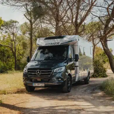 HYMER B-Klasse ModernComfort T Wohnmobil steht auf einem naturbelassenen Stellplatz im Grünen, umgeben von Bäumen