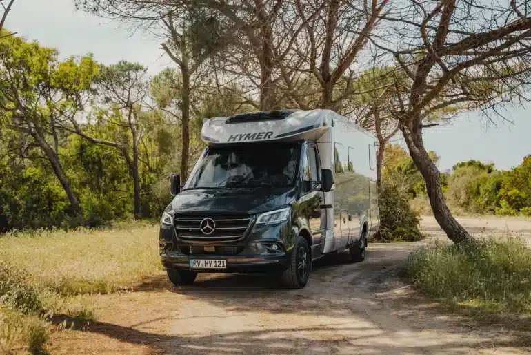 HYMER B-Klasse ModernComfort T Wohnmobil steht auf einem naturbelassenen Stellplatz im Grünen, umgeben von Bäumen