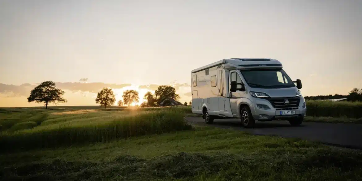 HYMER Exsis-t Pure Wohnmobil fährt bei Sonnenuntergang über eine Landstraße, umgeben von Feldern und Bäumen