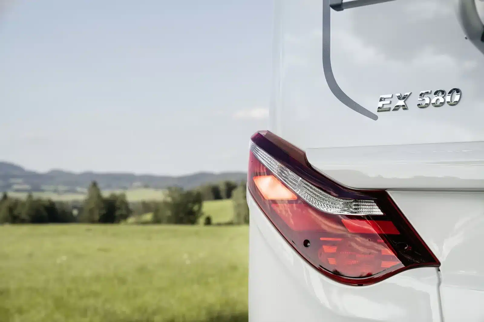 Rücklicht und Modellbezeichnung EX 580 eines HYMER Exsis-t Pure Wohnmobils mit grüner Landschaft im Hintergrund