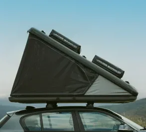 Seitliche Ansicht eines geöffneten James Baroud Nova L Hartschalen-Dachzelts in Dunkelgrau auf einem Fahrzeugdach vor Landschaft