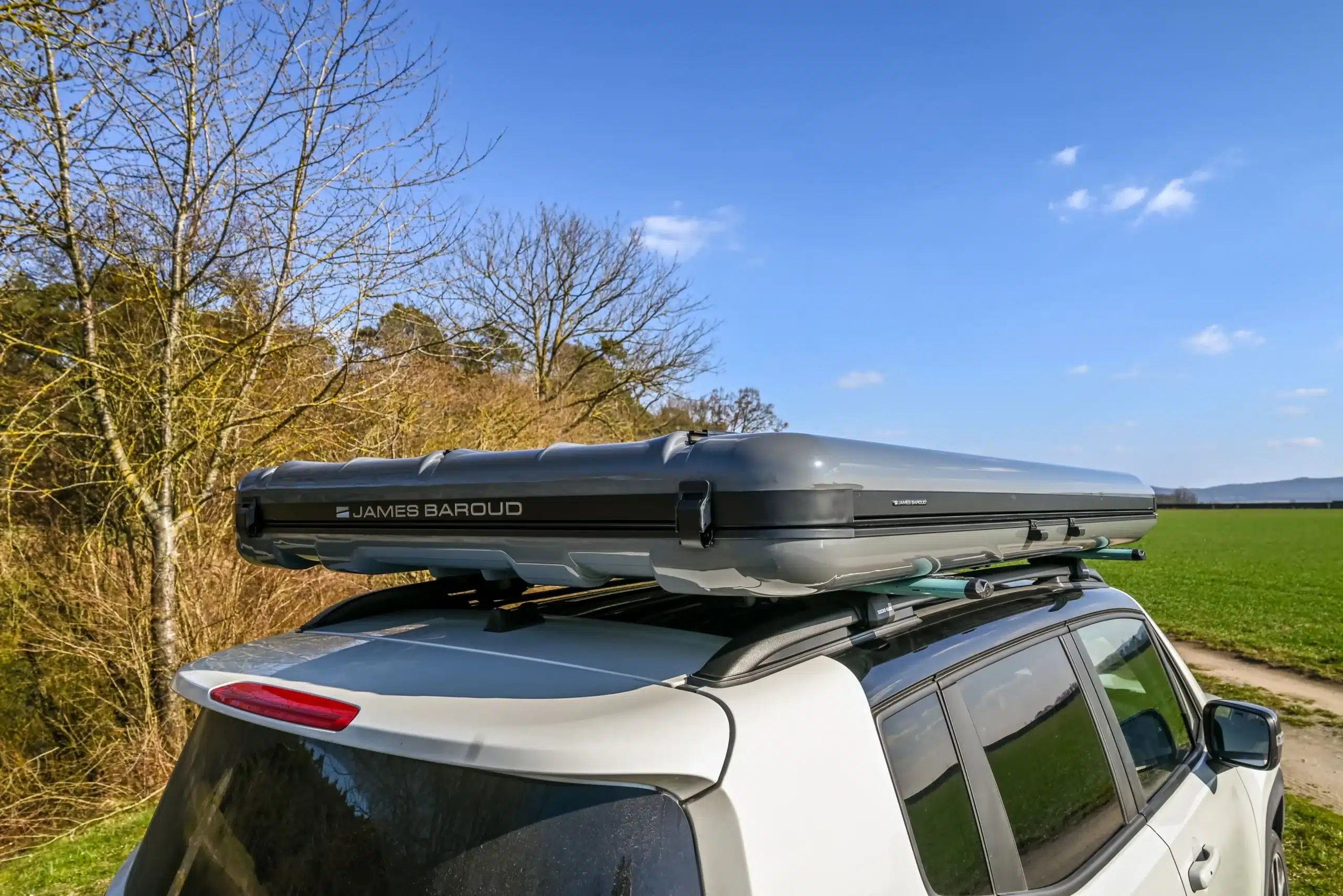 James Baroud Nova L Hartschalen-Dachzelt in Dunkelgrau montiert auf einem weißen Fahrzeug vor ländlicher Kulisse