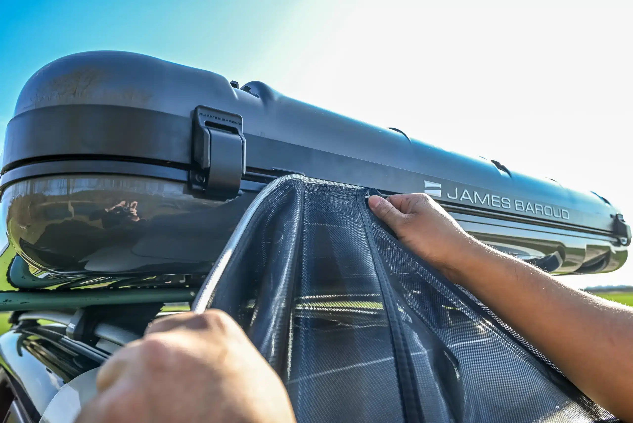 James Baroud Nova L Hartschalen-Dachzelt in Dunkelgrau auf einem Fahrzeugdach, Hände beim Öffnen des Zeltes