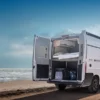 KNAUS BOXLIFE Camper Van mit geöffneten Hecktüren am Strand, Blick auf das flexible Innenraumkonzept und Stauraum