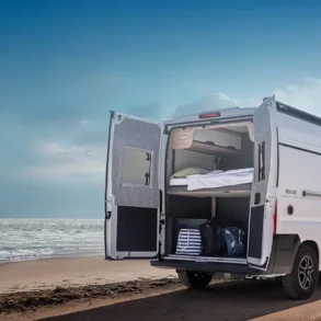 KNAUS BOXLIFE Camper Van mit geöffneten Hecktüren am Strand, Blick auf das flexible Innenraumkonzept und Stauraum