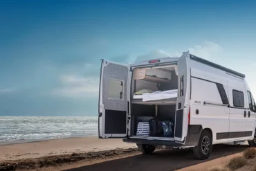 KNAUS BOXLIFE Camper Van mit geöffneten Hecktüren am Strand, Blick auf das flexible Innenraumkonzept und Stauraum